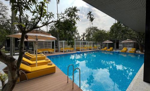 a large swimming pool with yellow lounge chairs and umbrellas at Glamp Wilderness in Nelamangala