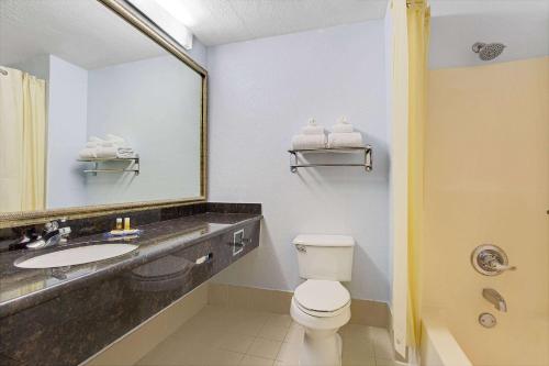 a bathroom with a toilet and a sink and a mirror at Days Inn by Wyndham Dallas Garland West in Garland