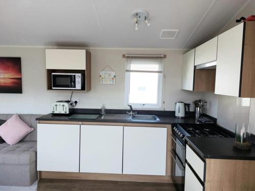 a kitchen with white cabinets and a stove top oven at Southview Holiday Park Skegness - Upgraded Caravan - Unica in Skegness