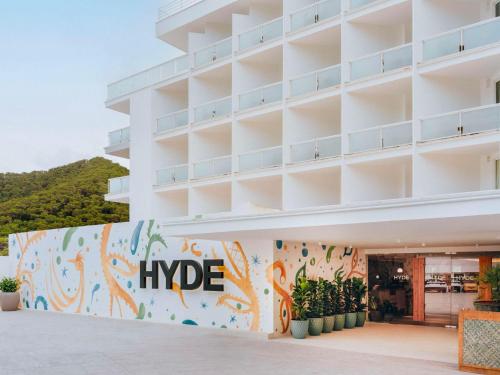 un grand bâtiment blanc avec une grande fresque sur le côté dans l'établissement Hyde Ibiza, à Cala Llonga