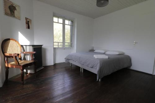 een slaapkamer met een bed, een stoel en een raam bij Maison dans le bourg, 6-8 couchages avec piscine in Groléjac