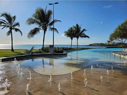 a fountain with palm trees in front of the ocean at ARay at Cooee Bay - Apt B - Beach House Yeppoon in Yeppoon