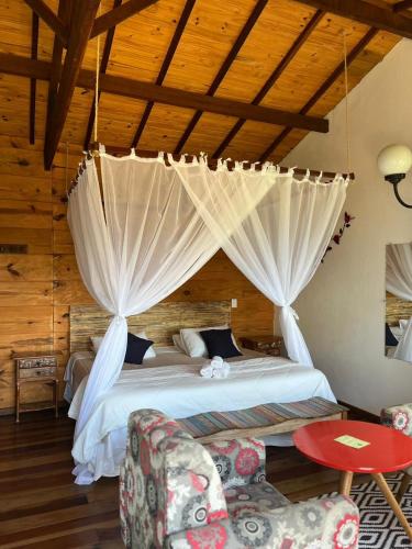 a bedroom with a bed with curtains and chairs at Pousada Sesmaria in Lavras Novas
