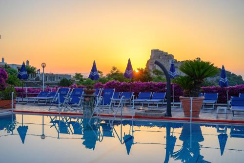 una piscina con sedie e un tramonto sullo sfondo di Hotel Parco Cartaromana a Ischia