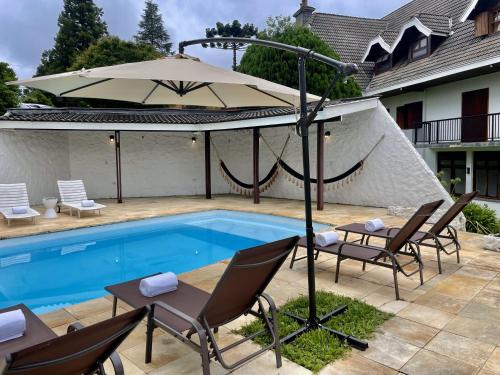a pool with chairs and an umbrella next to a house at Casa Três Rios - Campos do Jordão in Campos do Jordão