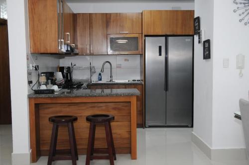 a kitchen with a stainless steel refrigerator and two stools at Tu penthouse en torre real Vl monumental in Santiago de los Caballeros
