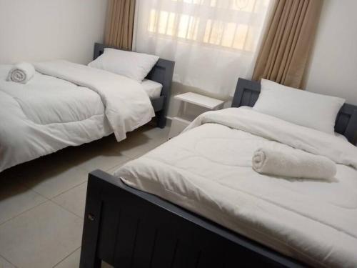 1 dormitorio con 2 camas con sábanas blancas y ventana en Luxurious Homes AthiRiver, en Athi River