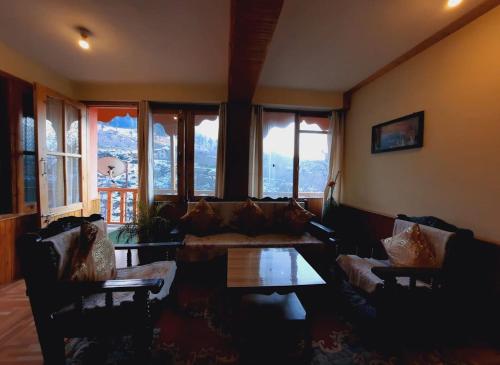 a living room with couches and a table and windows at Nest Villa Homestay in Nagar