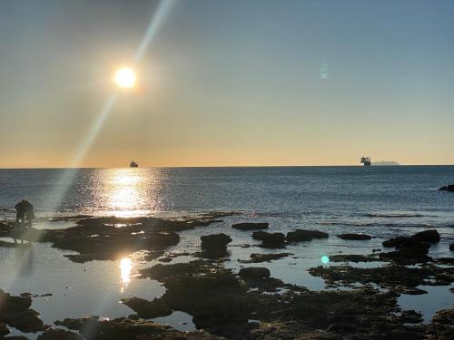 Słońce zachodzące nad oceanem z kamieniami w wodzie w obiekcie Casa vento marino w mieście Livorno