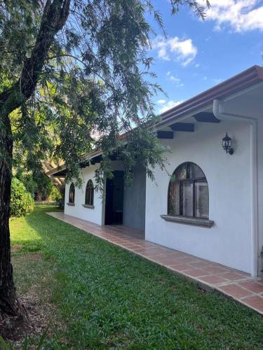 a white house with a tree and a lawn at Hacienda Escondida 10min to Airport in Alajuela City