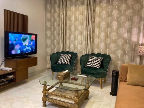a living room with two green chairs and a tv at Homey Stays - 3 Bedroom Holiday Home - DHA in Lahore