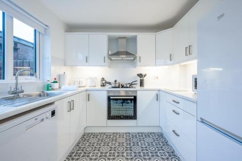 a white kitchen with white cabinets and a sink at Walk to City Centre Townhouse, Garden and Parking by StayByNumbers in Belfast