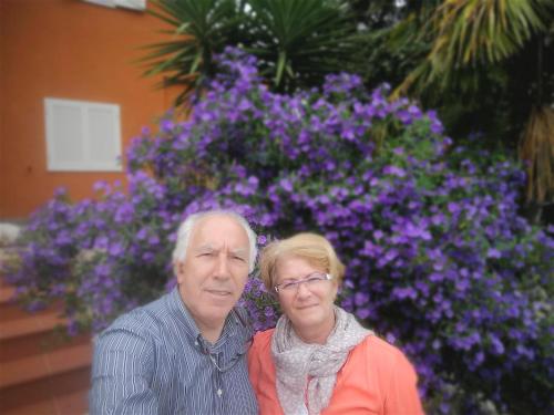 an older man and woman standing in front of purple flowers at Da Zia Piera in Castelnuovo di Porto