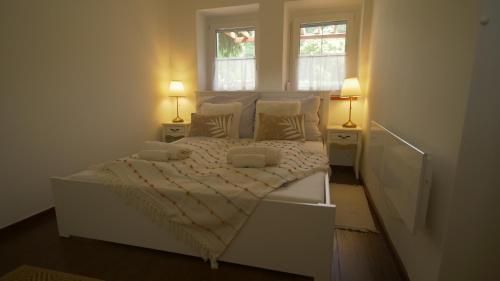 a white bedroom with a bed and two windows at Kapolcs Vendégház in Kapolcs