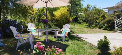 3 sillas y una mesa con sombrilla en un jardín en Hospedaje Brisas de Frutillar en Frutillar