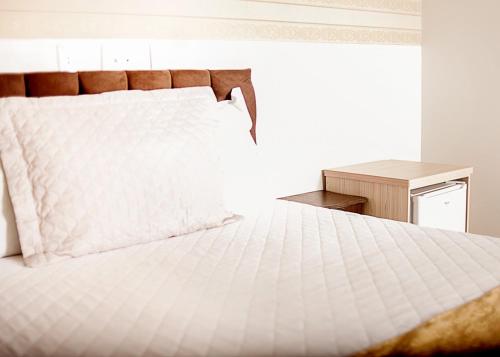 um quarto com uma cama branca e uma mesa de cabeceira em Hotel Grezelle em Santa Bárbara
