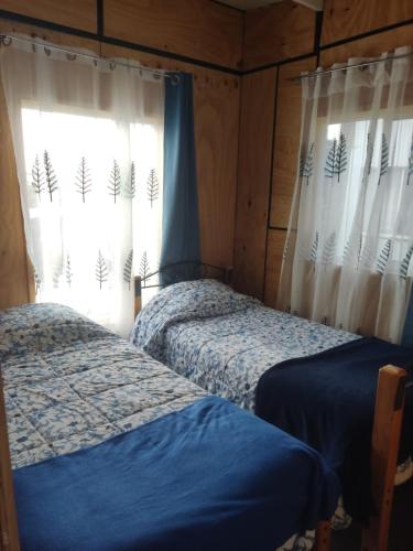 1 dormitorio con 2 camas y una ventana con cortinas en Cabaña Chaitén en Chaitén