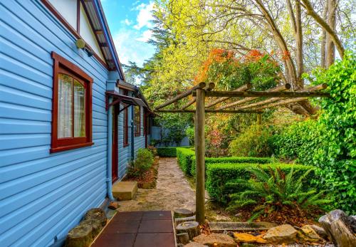 a pathway leading to a blue house with a wooden arbor at KUBBA ROONGA GUESTHOUSE - Boutique Luxury Spa Retreat & Gardens - Blue Mountains in Blackheath