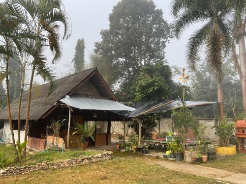 a house with a gambrel roof and palm trees at Adinda house อดินดาเฮาส์ in Chiang Dao