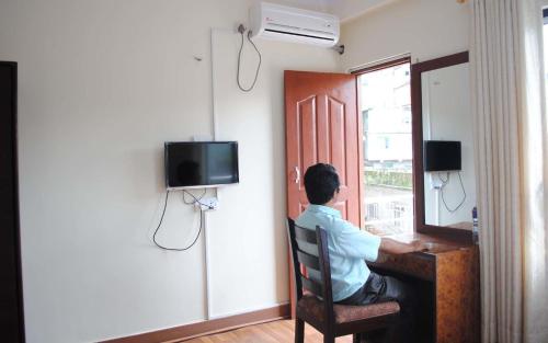 un hombre sentado en un escritorio en una habitación con ventana en Avalon House, en Katmandú