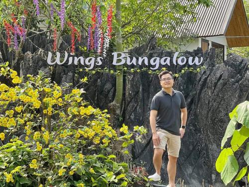 Un uomo in piedi davanti a un cartello con dei fiori di Ha Giang Wings Bungalow a Ha Giang