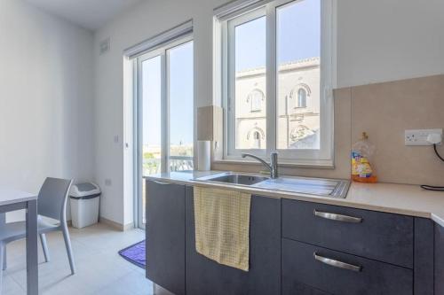een keuken met een wastafel en een tafel en een aantal ramen bij Full Air-conditioned, 2 Bedroom Apt. in Żejtun