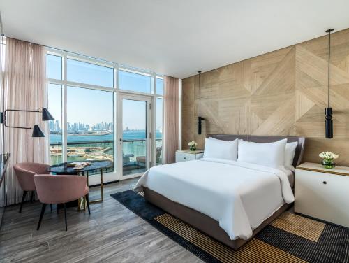a bedroom with a large white bed and a desk and a large window at Rixos Gulf Hotel Doha in Doha
