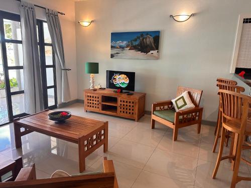ein Wohnzimmer mit einem TV, einem Tisch und Stühlen in der Unterkunft Cabanes Des Anges in La Digue