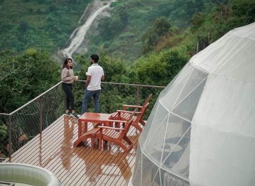 a man and woman standing on a deck looking at a waterfall at LUXEGLAMP ECOSTAYS in Kūkkāl