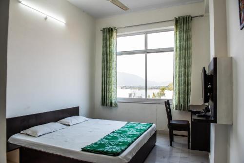 a bedroom with a bed and a desk and a window at Hotel Shivam in Ajmer