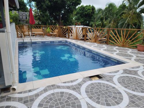 a swimming pool on a tiled patio with a fence at Le Longani in Rivière