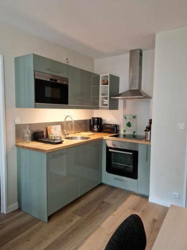 - une cuisine avec des placards bleus, un évier et une cuisinière dans l'établissement Joli appartement avec balcon, à Cabourg