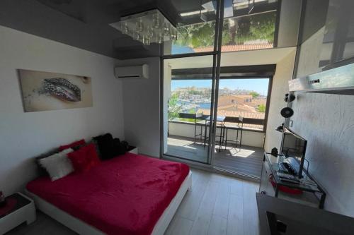 une chambre avec un lit rouge et une grande fenêtre dans l'établissement Naturiste Cap d'Agde Port Vénus 206, au Cap d'Agde