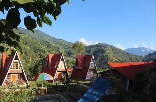 a group of houses with red roofs with mountains in the background at Orchard Farmstay in Bijanbāri Bāzār
