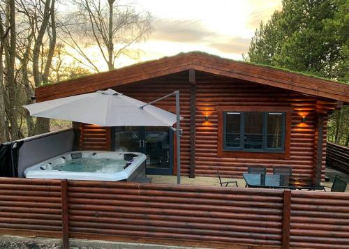 a small cabin with a hot tub and an umbrella at Beech Hedge in Coupar Angus