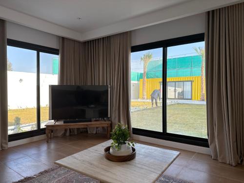 ein Wohnzimmer mit einem Flachbild-TV und großen Fenstern in der Unterkunft container chalet in Buraida