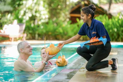 a man in a swimming pool with a woman holding fruit in the pool at Athgira River Camping - Udawalawe in Udawalawe