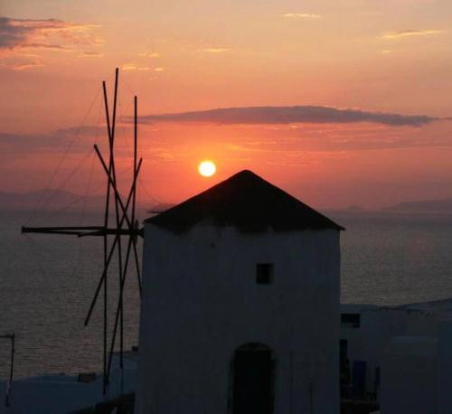 a sunset with a windmill in front of the ocean at Lioyerma Windmill Villa With Outdoor Hot Tub in Oia