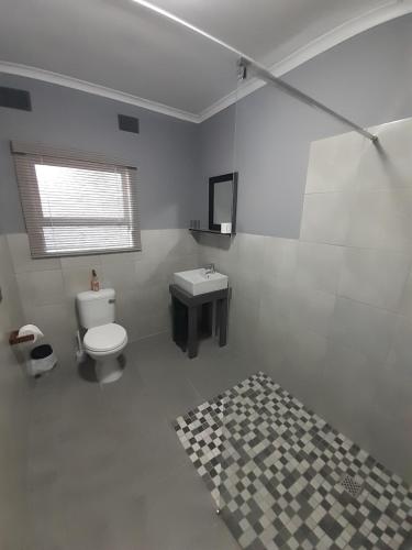 a white bathroom with a toilet and a sink at Honeysuckle Manor in Richards Bay