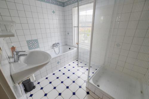 Baño de azulejos blancos con lavabo y bañera en Herenhuis de Pastorie Groede, en Groede