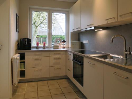 d'une cuisine avec des placards blancs, un évier et une fenêtre. dans l'établissement Ferienhaus Süder-Tresker, à Tinnum