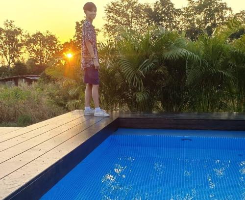 a young child standing on a wooden deck near a swimming pool at ฺBaannoi in the garden บ้านน้อยกลางทุ่ง Pool villa 