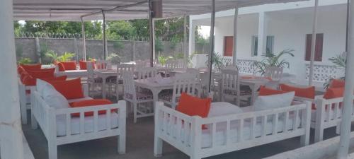 a patio with white tables and chairs with red pillows at Butah Gardens Watamu in Gede