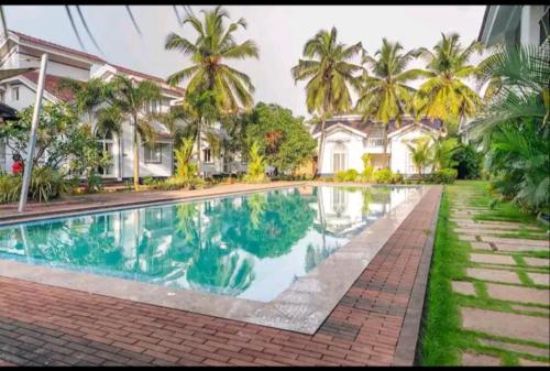 a swimming pool in front of a house with palm trees at Riviera Sublime Holiday Homes in Siolim