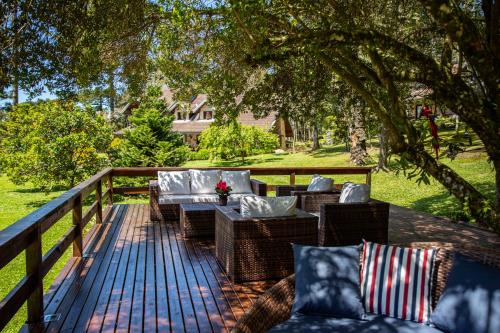 a deck with wicker chairs and tables under a tree at Estalagem Coração Da Mata in Gramado