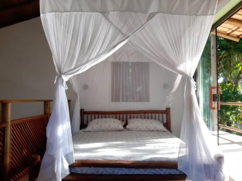 um quarto com uma cama de dossel e cortinas brancas em Boutique Beach Chalet, Luzimares, Serra Grande-BA em Serra Grande