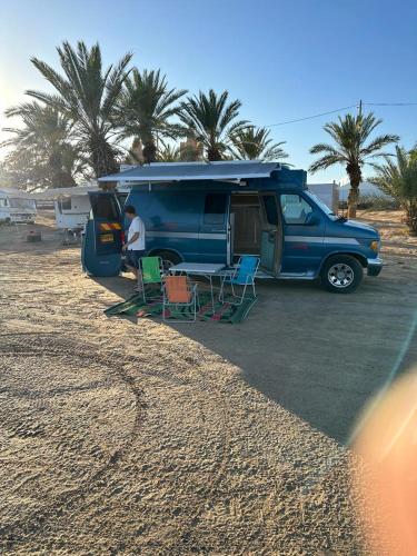 niebieski van zaparkowany na plaży ze stołem i krzesłami w obiekcie הקראוון של תומר w Ejlat