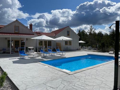 a pool with chairs and umbrellas in front of a house at Villa Vitviken Sleeps 4 with Pool in Slite