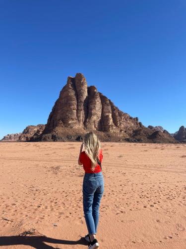 Una donna in piedi di fronte a delle formazioni rocciose di Zarb Desert Camp a Wadi Rum