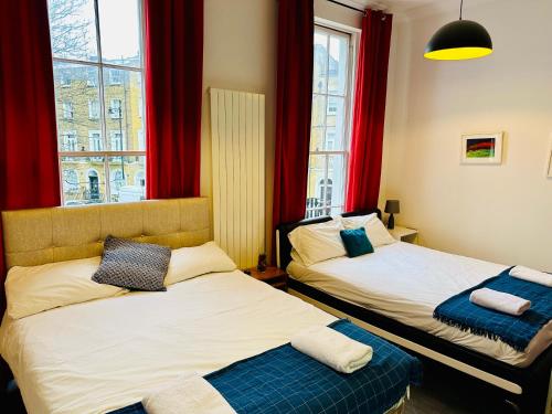 2 camas en una habitación con cortinas rojas en London Regent Studio Apartments en Londres